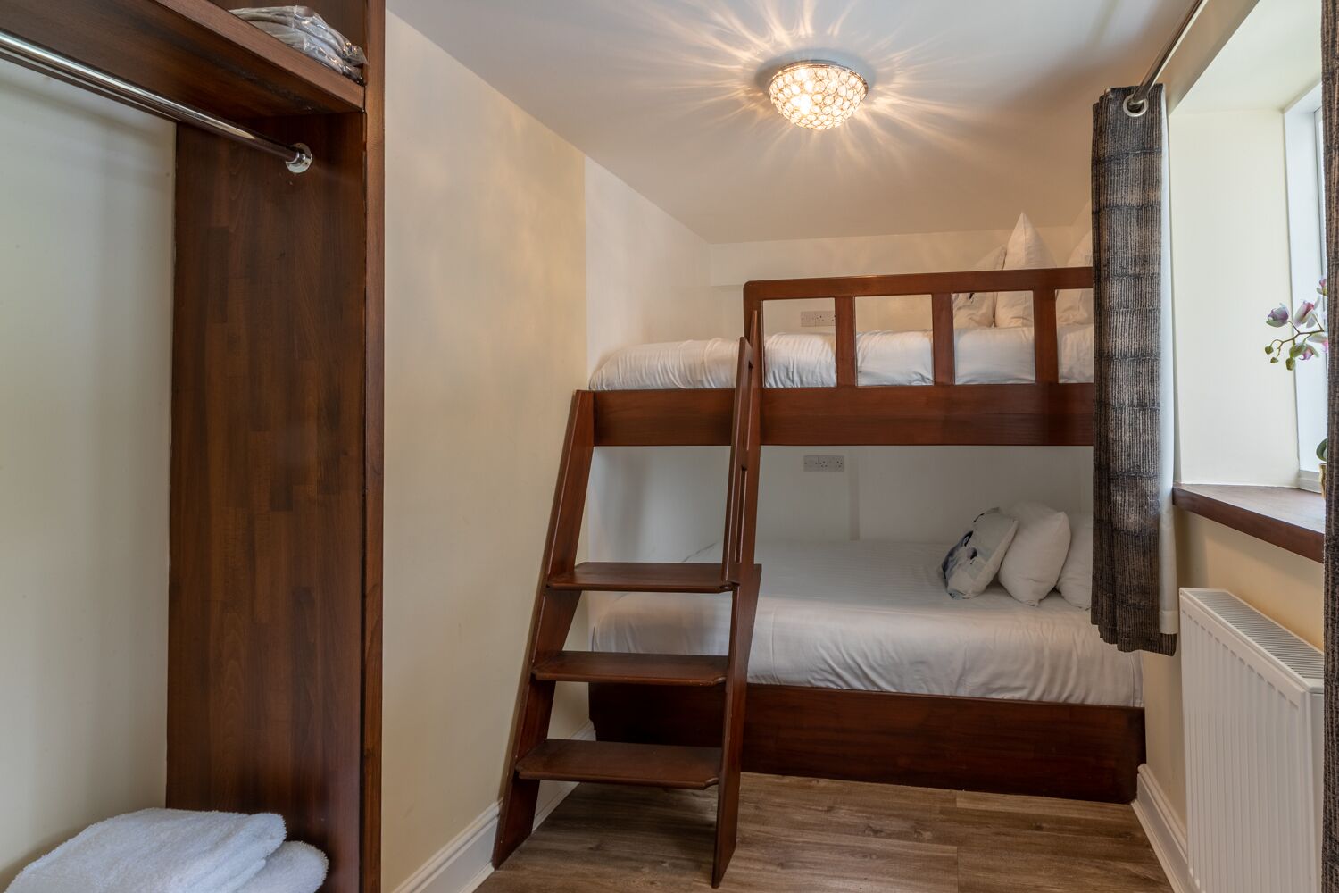 Een slaapkamer met een stapelbed, een houten trapje, een radiator en een plank met een handdoek.