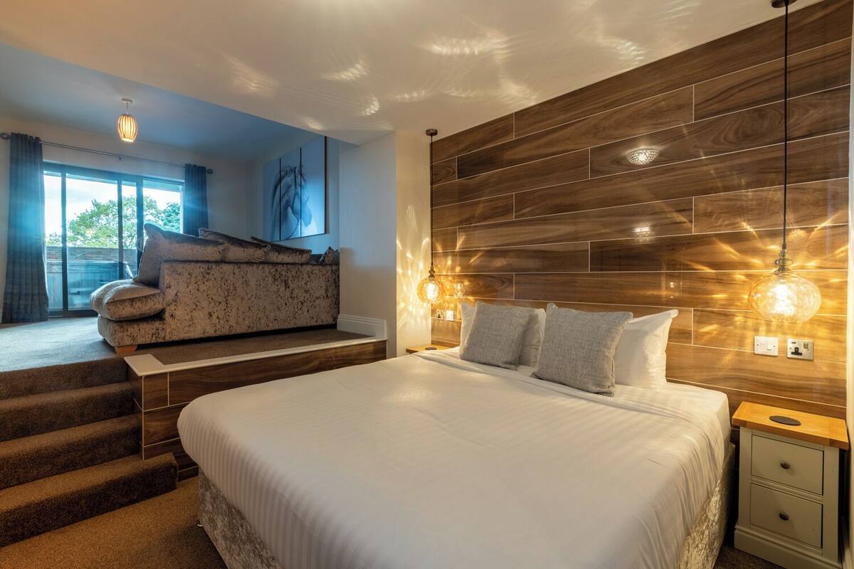 A modern bedroom with a large bed, a wooden headboard, and a staircase leading to an upper level.