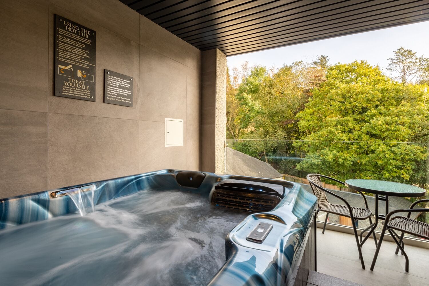 A hot tub with a control panel, surrounded by a patio area with chairs and a table.