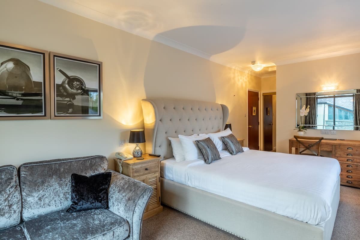 A bedroom with a large bed, a nightstand with a lamp, a chair, and two framed pictures on the wall.