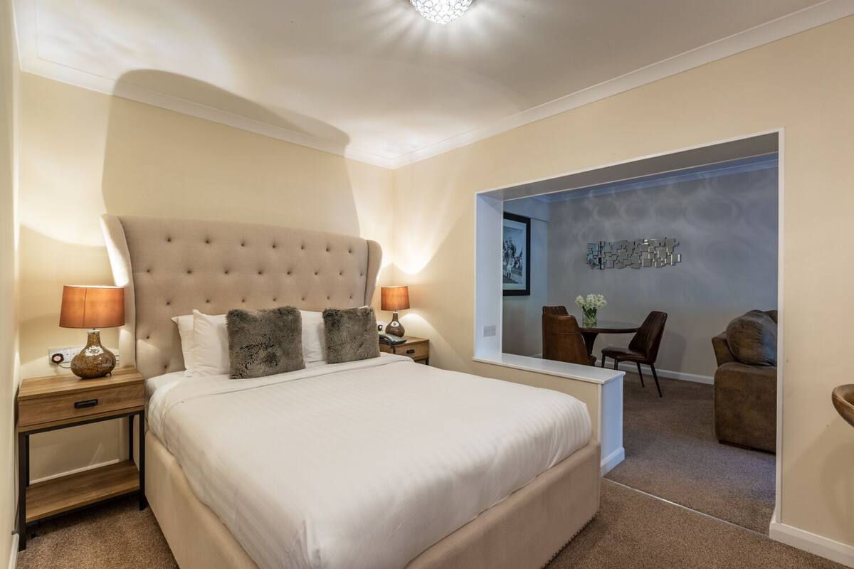 A bedroom with a large bed, two bedside tables with lamps, a mirror, and a seating area with a table and chairs.