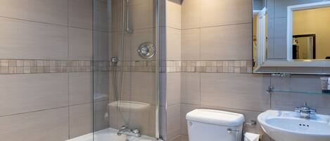 A modern bathroom with a glass-enclosed shower, a white bathtub, a toilet, and a sink with a mirror above it.