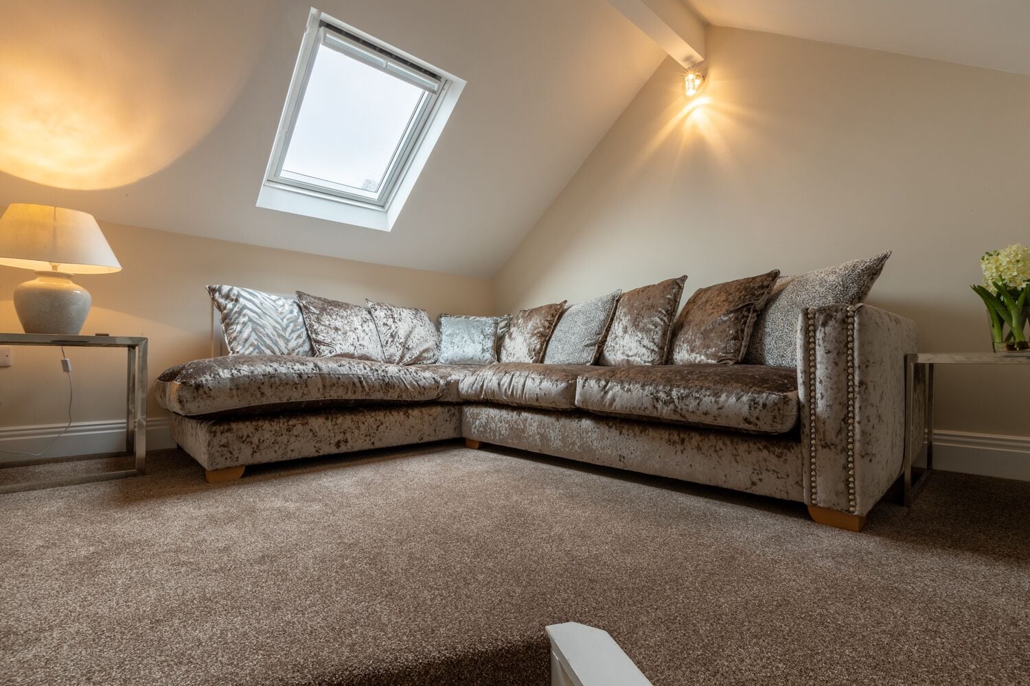 A corner living room with a sectional sofa, a lamp, a small table, and a skylight.