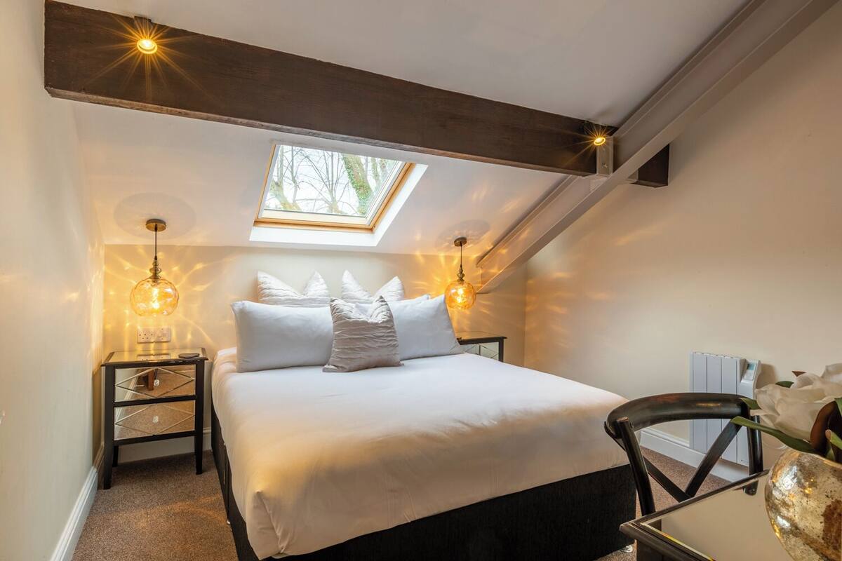 A bedroom with a skylight, a bed with white bedding, two bedside tables with lamps, and a chair.