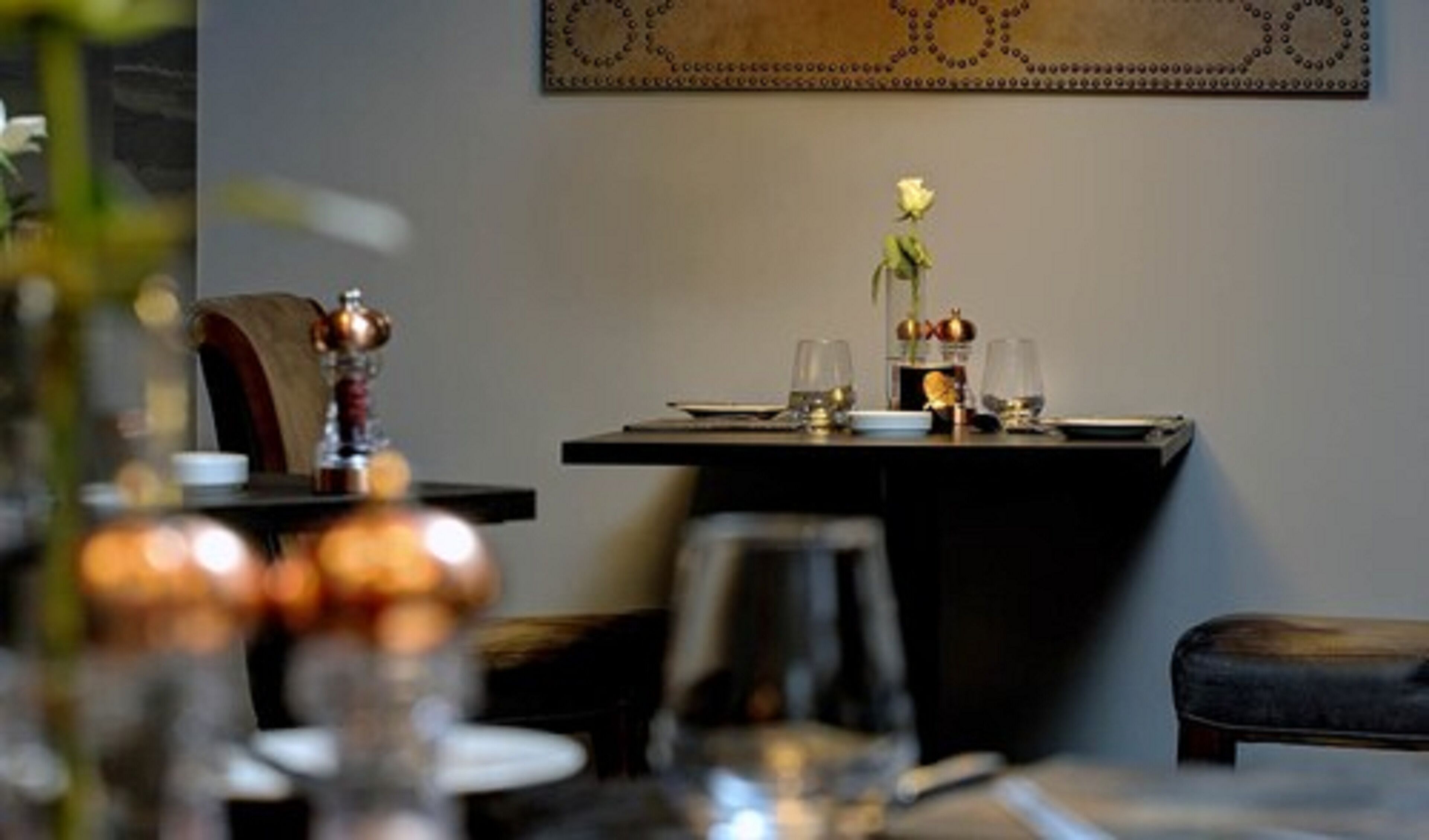 Une table à manger dressée avec des verres, un vase contenant une seule fleur et un objet décoratif.