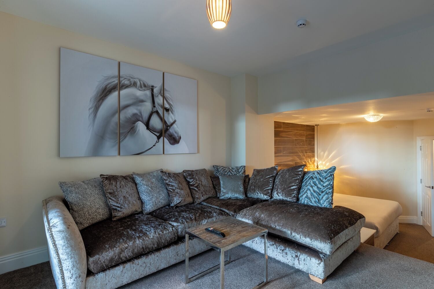 A modern living room with a sectional sofa, a coffee table, and a large horse-themed artwork on the wall.