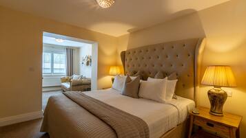 A hotel room with a large bed, two bedside lamps, a wooden nightstand, and a view of a dining area.