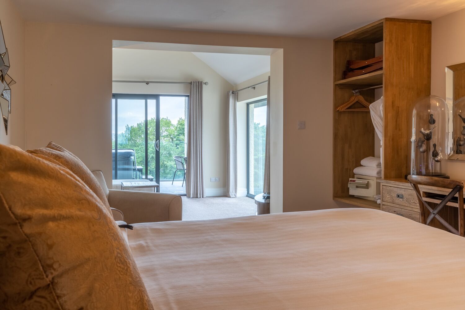 A hotel room with a large bed, a wooden wardrobe, a desk, and a view of the outdoors through the window.