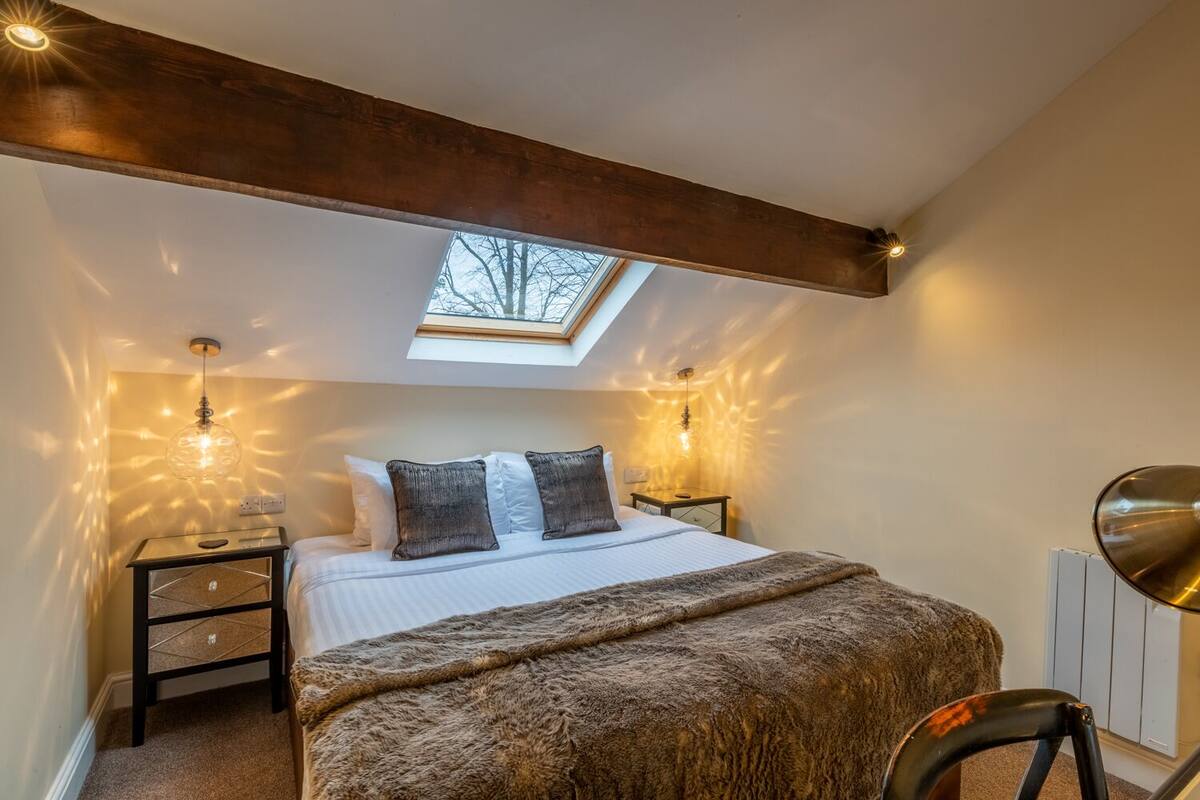 A bedroom with a skylight, a bed with a fluffy blanket, two bedside tables with lamps, and a chair.