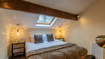 A bedroom with a skylight, a bed with a fluffy blanket, two bedside tables with lamps, and a chair.