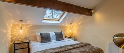 A bedroom with a skylight, a bed with a fluffy blanket, two bedside tables with lamps, and a chair.