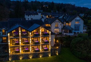 A hotel with multiple balconies, each with seating and lighting. The building has a stone facade and is surrounded by a well-maintained lawn. - Lakes Hotel and Spa (Windermere)