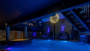 Zona d'una piscina interior moderna amb una gran llum en forma de cor il·luminada, parets de pedra i una escala que condueix a nivells superiors.