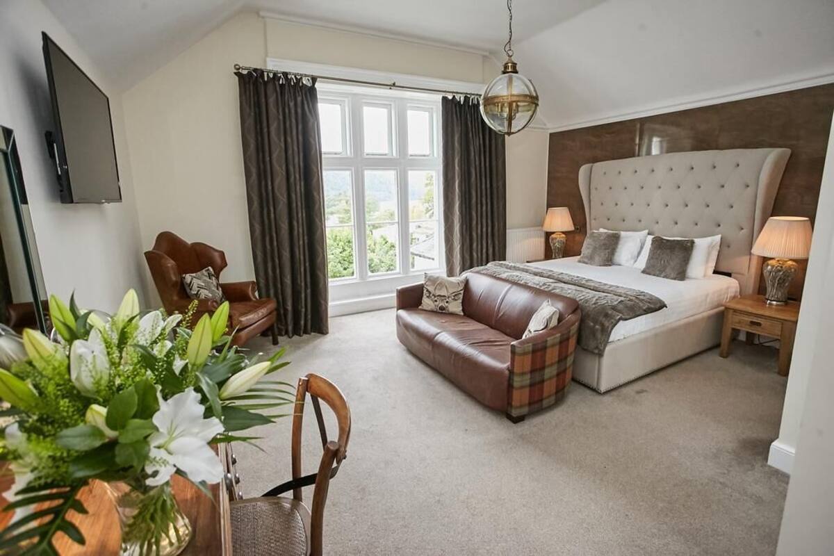 A bedroom with a large bed, a sofa, a chair, a TV, and a window with curtains.