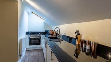 A compact kitchen with a built-in oven, a sink, and a coffee machine.