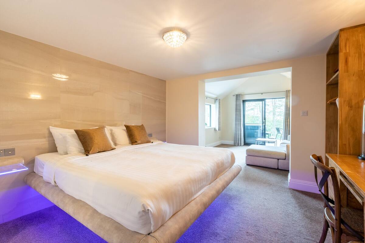 A modern bedroom with a large bed, a wooden desk, and a view of a balcony.