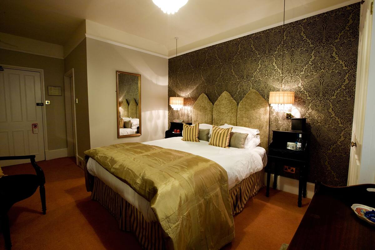 Ein Hotelzimmer mit einem großen Bett, einem Nachttisch mit Lampe, einem Sessel und einem Schminktisch.