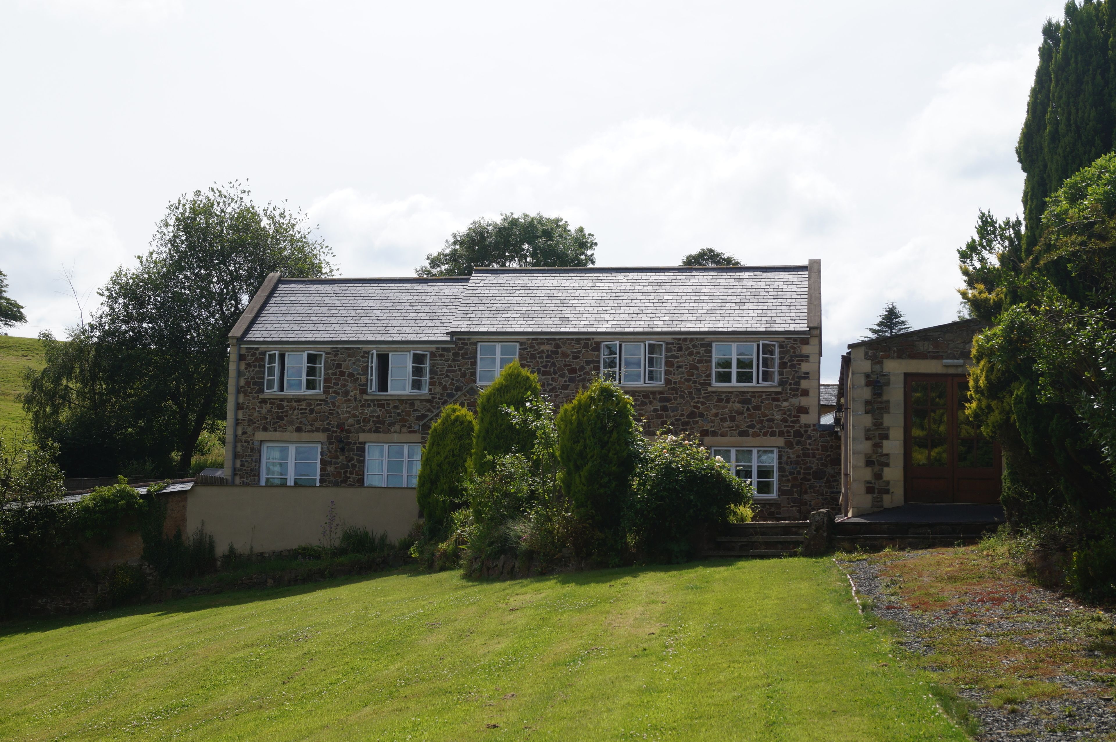 A two-story stone house with a sloped roof, a front porch, and a well-maintained lawn.