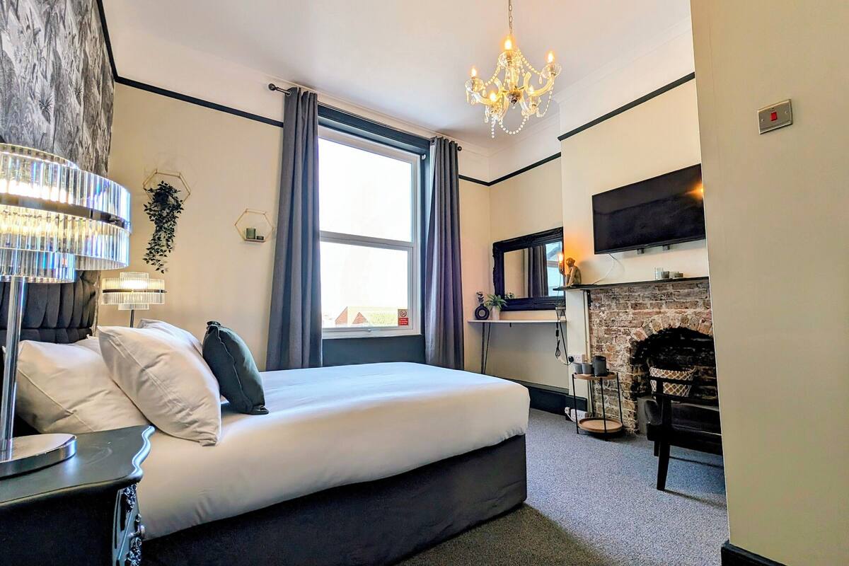 A hotel room with a bed, a chandelier, a fireplace, and a TV.