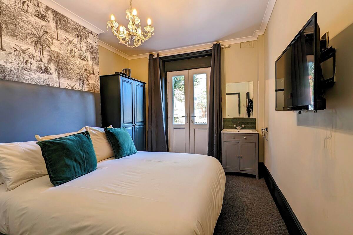 A hotel room with a large bed, a chandelier, a television, and a view of the outdoors through a door.