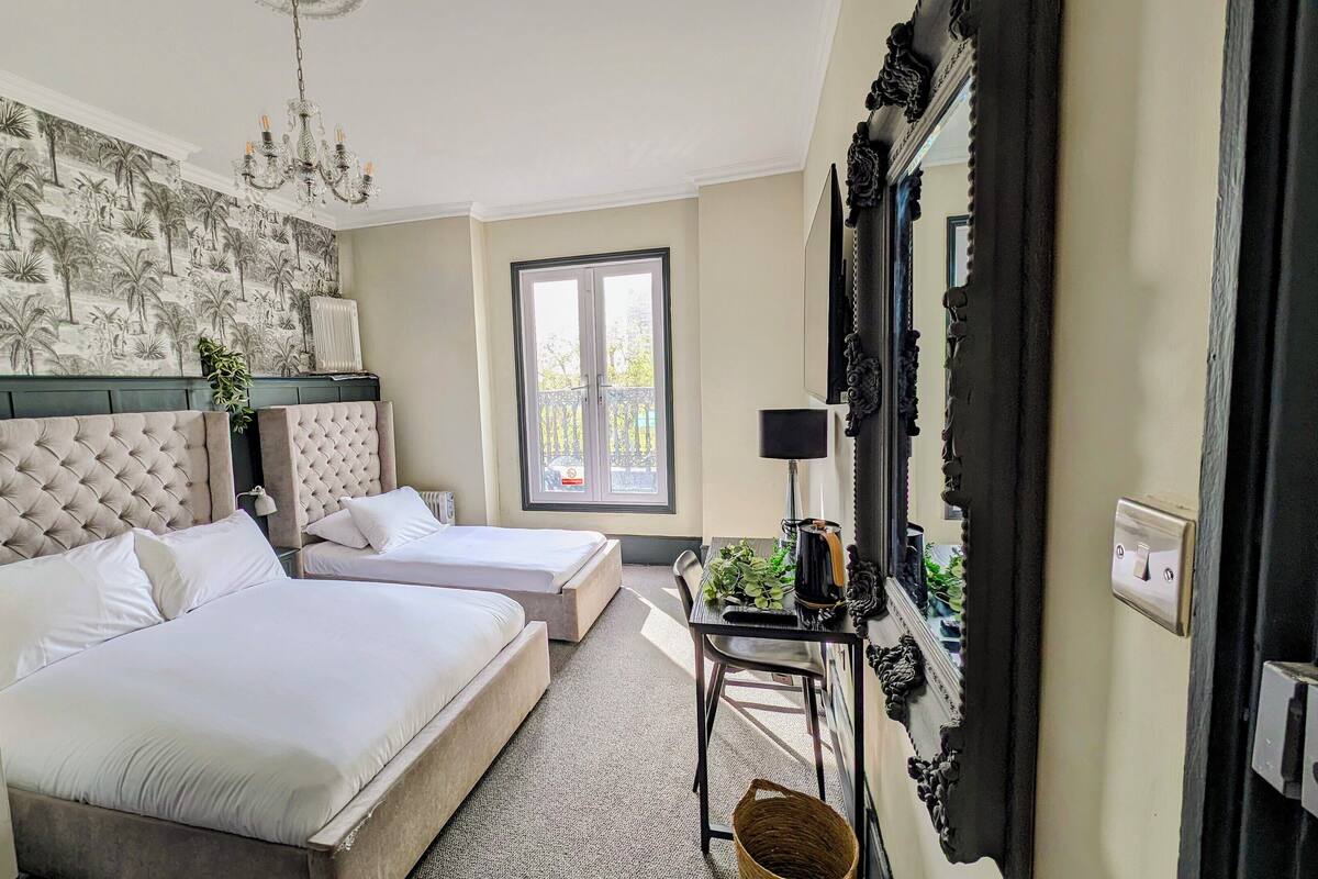A hotel room with two beds, a large mirror, a chandelier, and a window with a view of the outside.