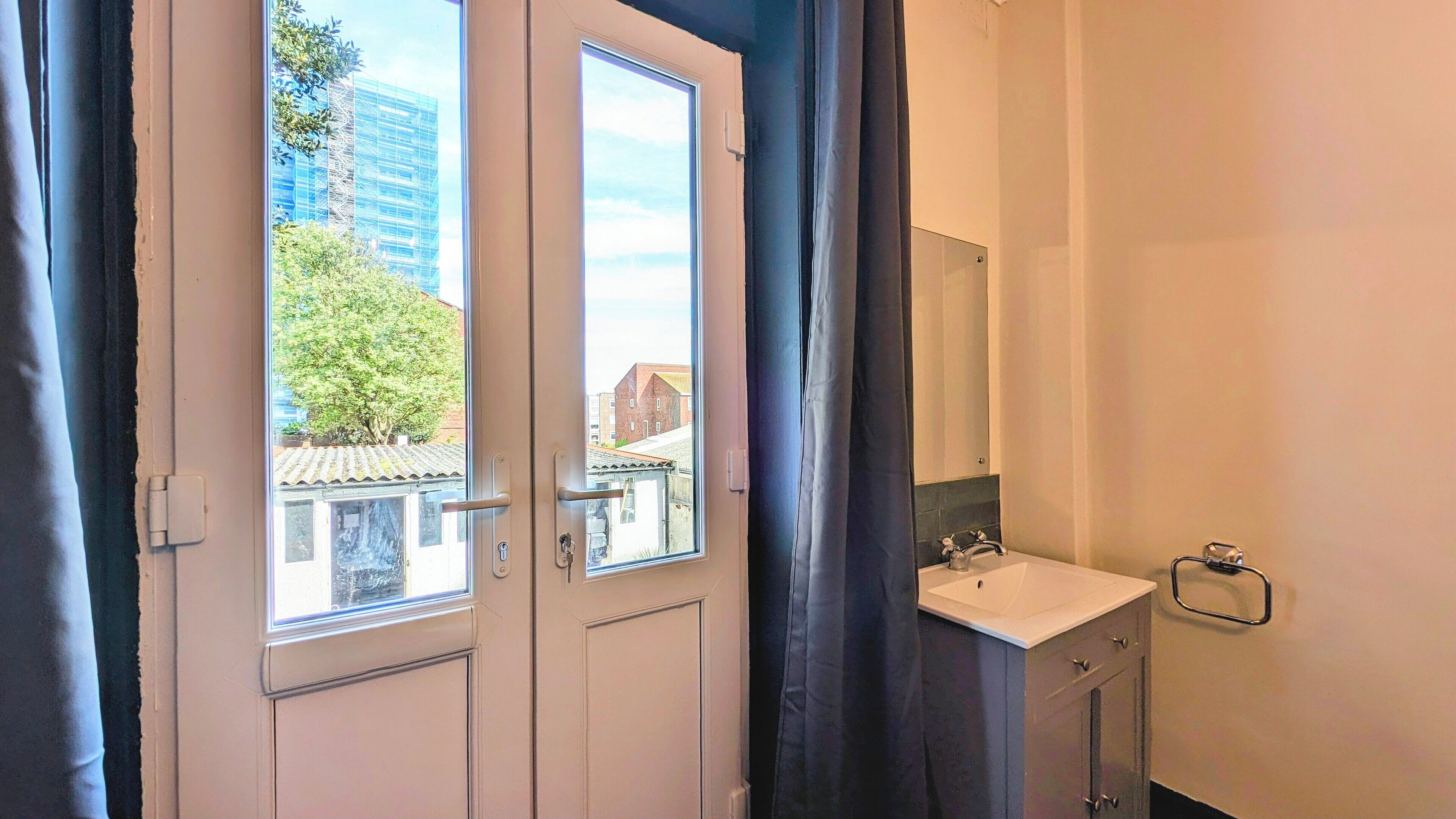 Un baño con lavamanos, espejo y vistas a edificios y árboles.