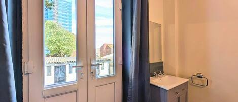 Un baño con lavamanos, espejo y vistas a edificios y árboles.