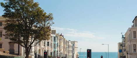 A coastal street with buildings, a tree, and a view of the sea.