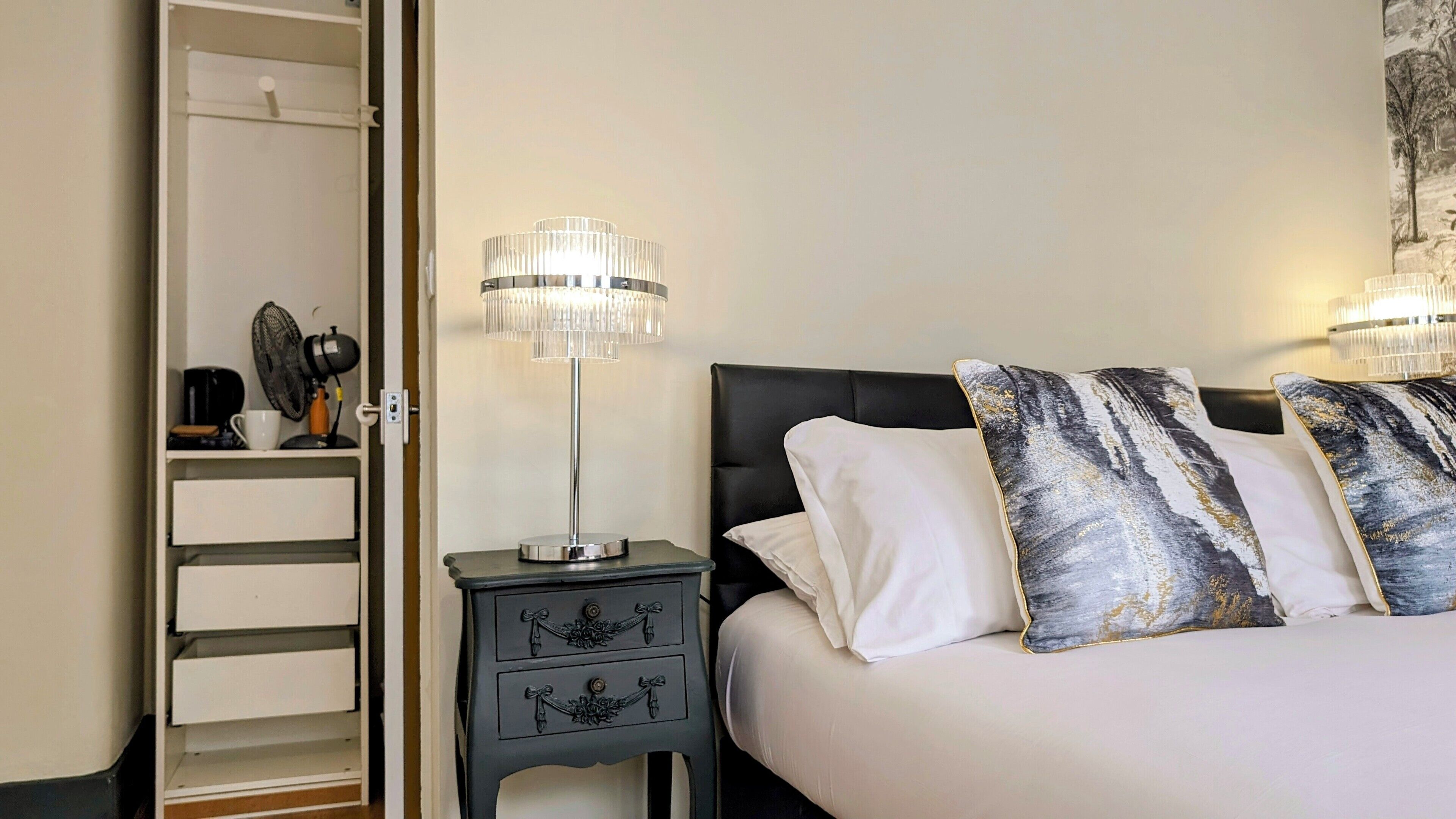 A bedroom with a bed, two bedside lamps, a nightstand, a closet, and a wall-mounted artwork.