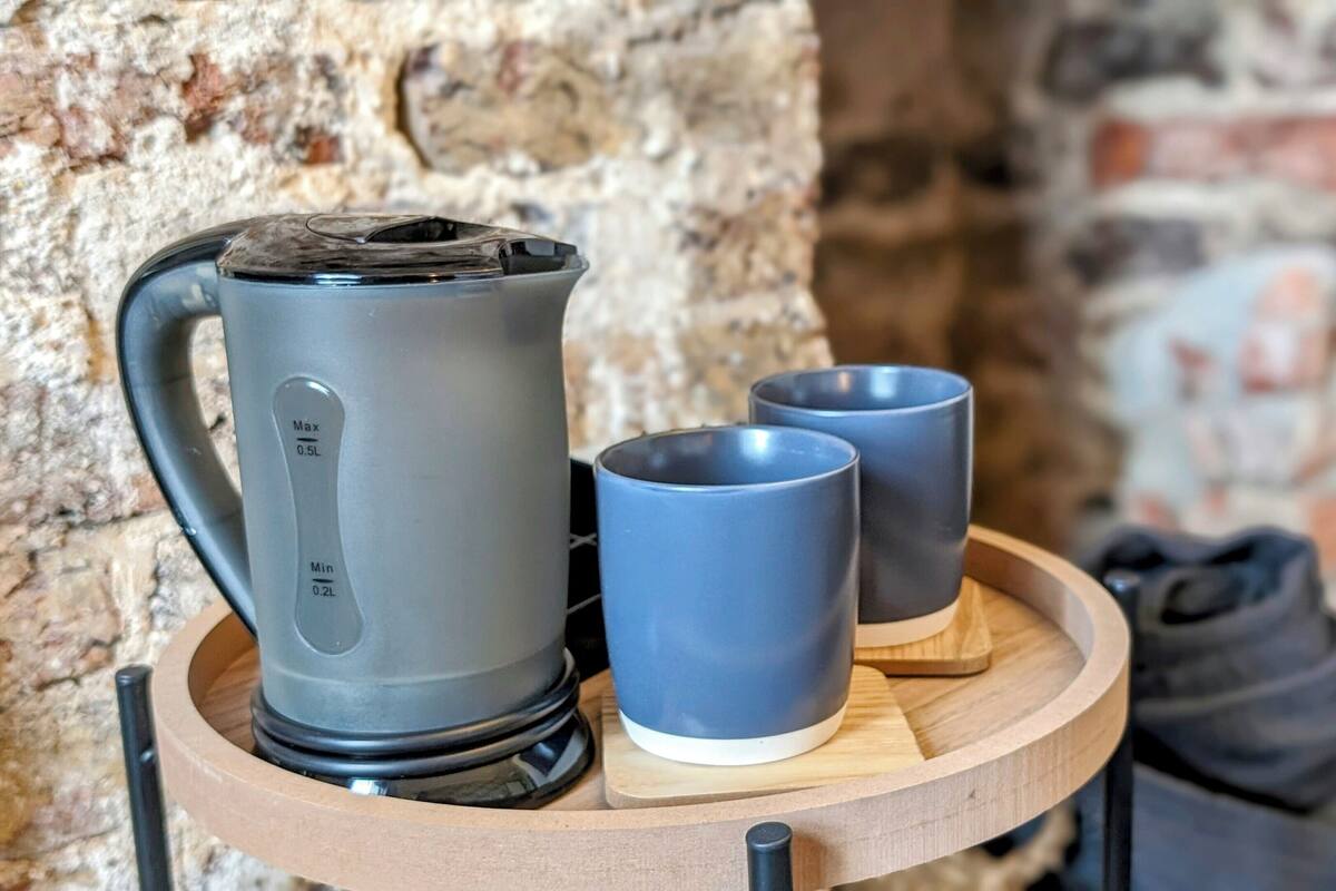 A kettle and two mugs on a wooden tray against a stone wall.