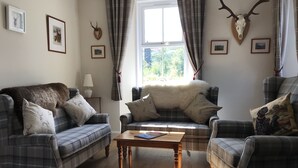 A cozy living room with plaid furniture, a wooden coffee table, and a deer skull mounted on the wall. - The Struan Inn Self Catering Lodge (Pitlochry)