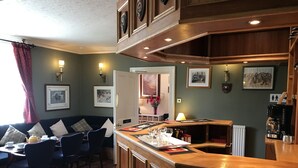 A cozy room with a wooden bar, a dining area with chairs and a table, and a sofa. - The Struan Inn Self Catering Lodge (Pitlochry)