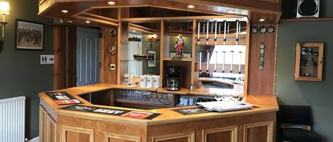 A bar area with wooden paneling, a coffee machine, and various bar tools. There are framed certificates on the wall and a mirror reflecting the bar area.