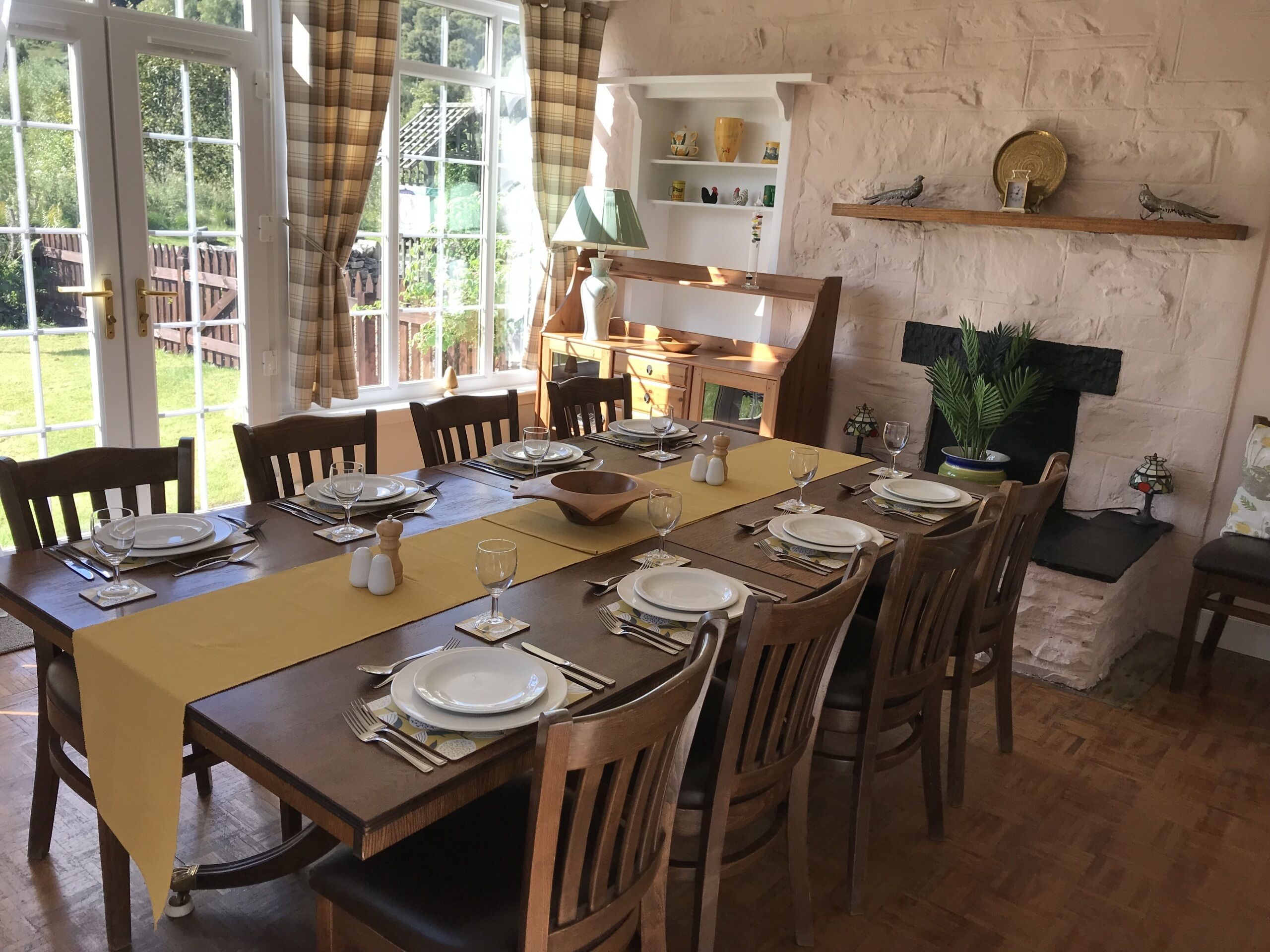 Un espace repas avec une longue table en bois, dressée pour six personnes, entourée de chaises en bois.