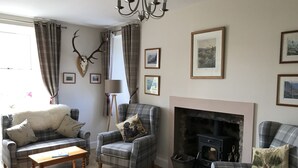 A cozy living room with plaid furniture, a fireplace, and wall-mounted deer antlers. - The Struan Inn Self Catering Lodge (Pitlochry)