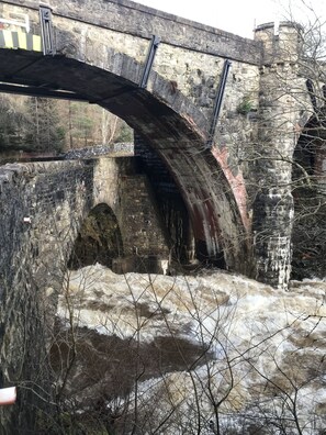 A stone bridge over a river with a rocky riverbed and bare trees in the foreground.