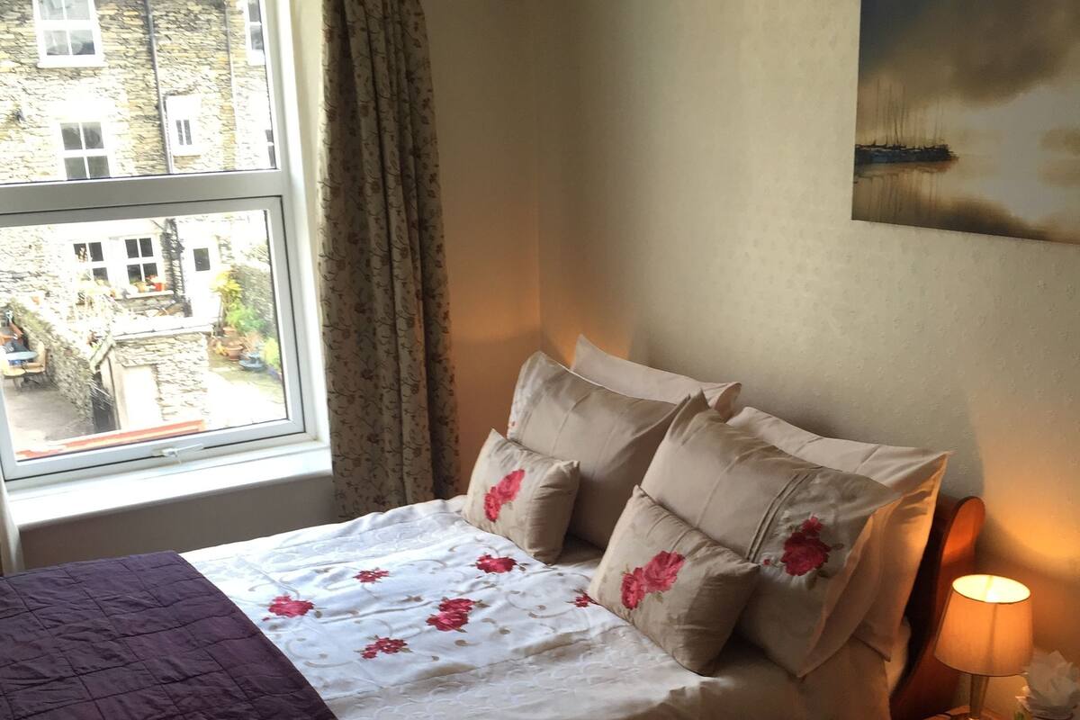 A neatly made bed with floral bedding, a bedside lamp, and a window with curtains.