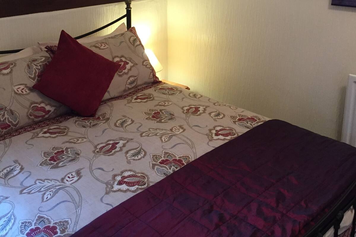 A bedroom with a bed, a red pillow, and a wooden headboard. There are three framed pictures on the wall.