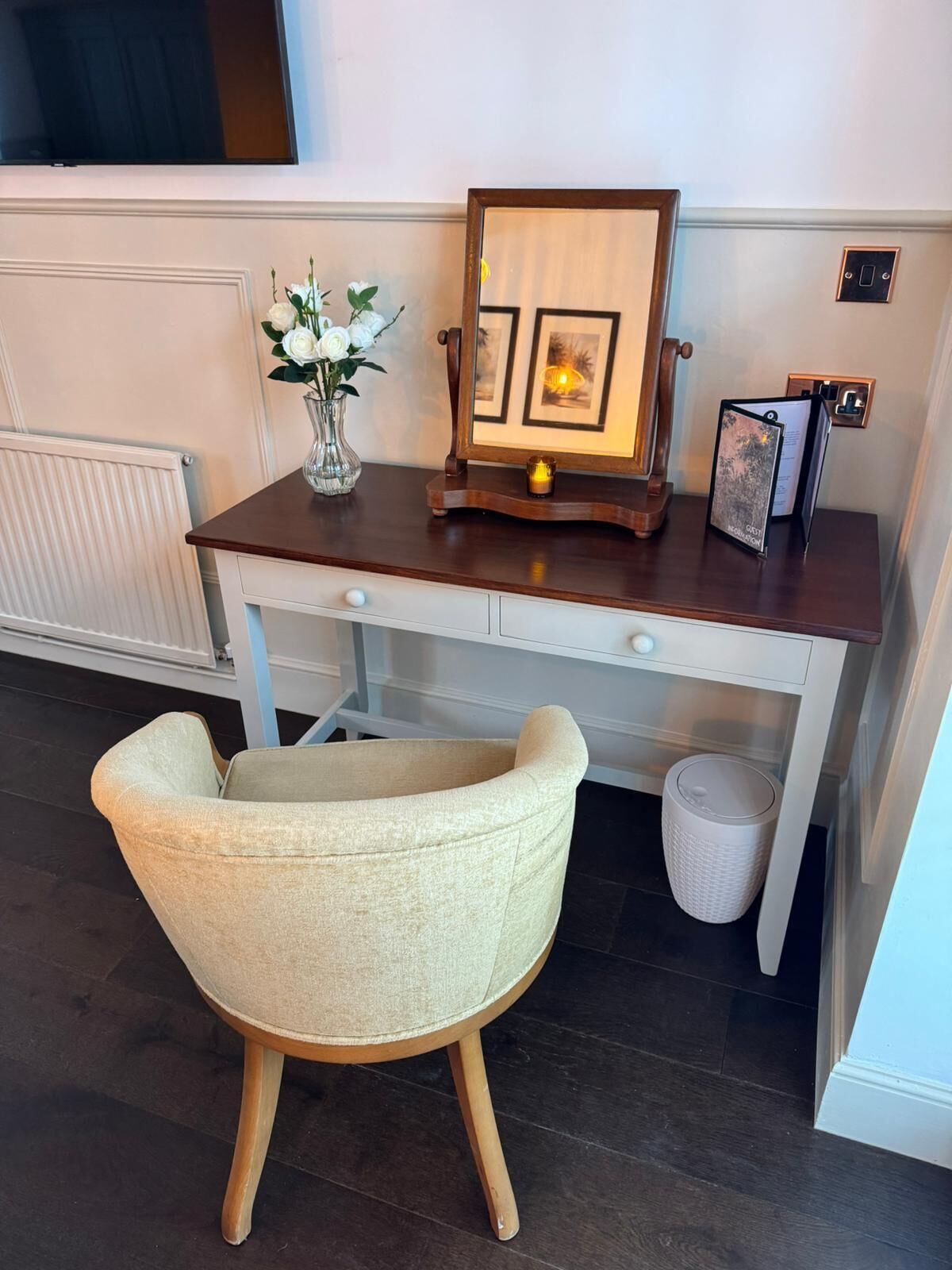 A wooden desk with a vase of white flowers, a framed picture, and a small candle.
