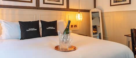 Et hotelværelse med en stor seng, champagneflaske og glas på et fad, indrammede billeder på væggen og et spejl.