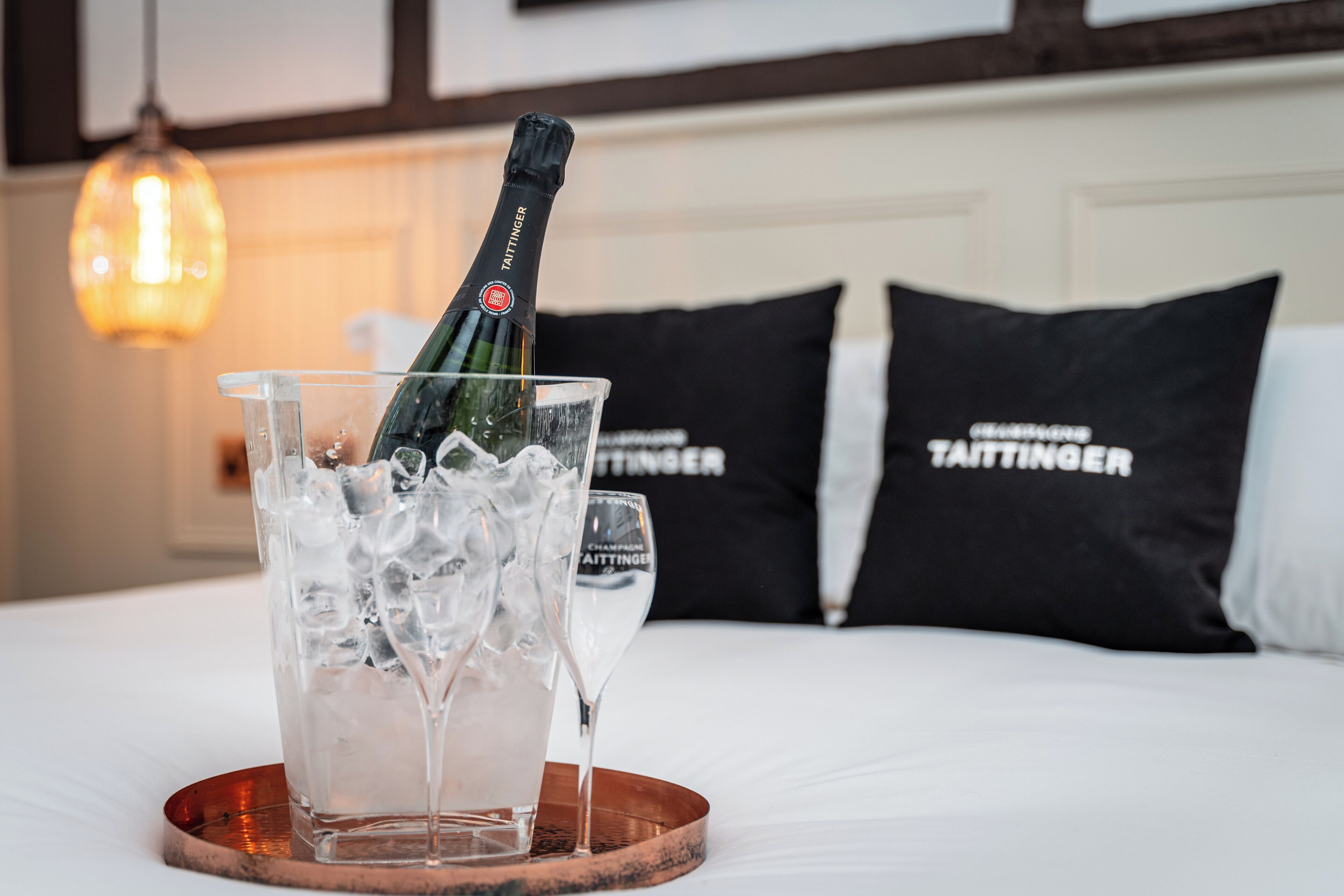 Un lit avec une bouteille de champagne dans un verre, des glaçons et une assiette. On peut voir deux oreillers portant le nom de la marque.