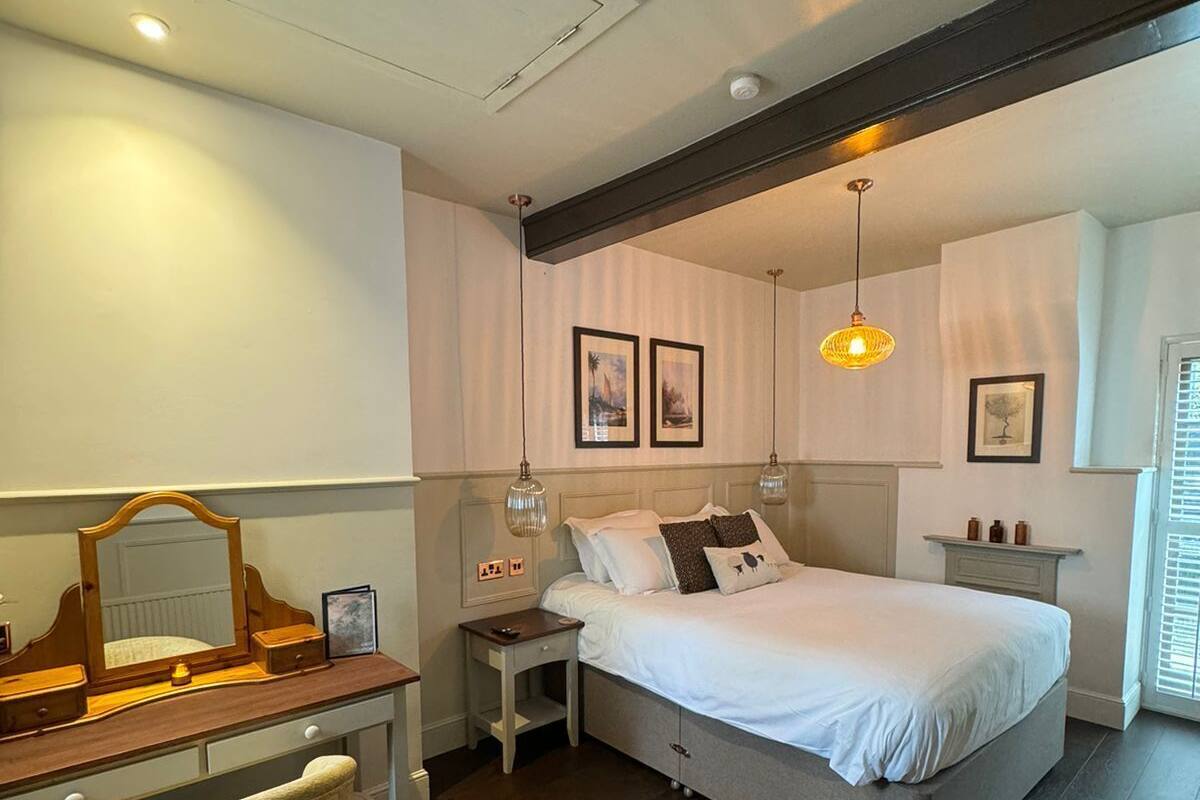 A bedroom with a bed, bedside table, dresser, chair, and a ceiling light fixture.