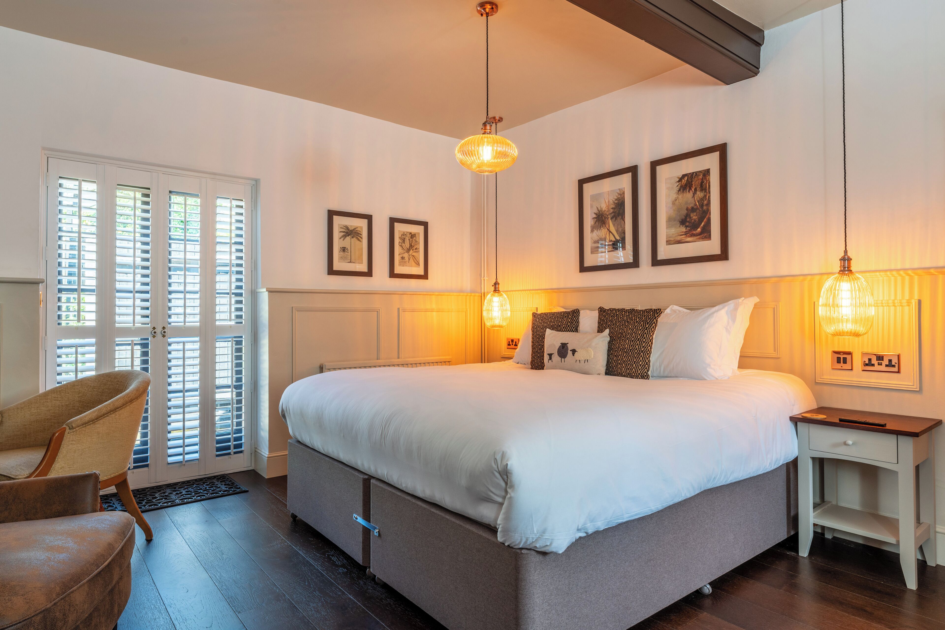 A bedroom with a large bed, a chair, a nightstand, and a door with shutters.