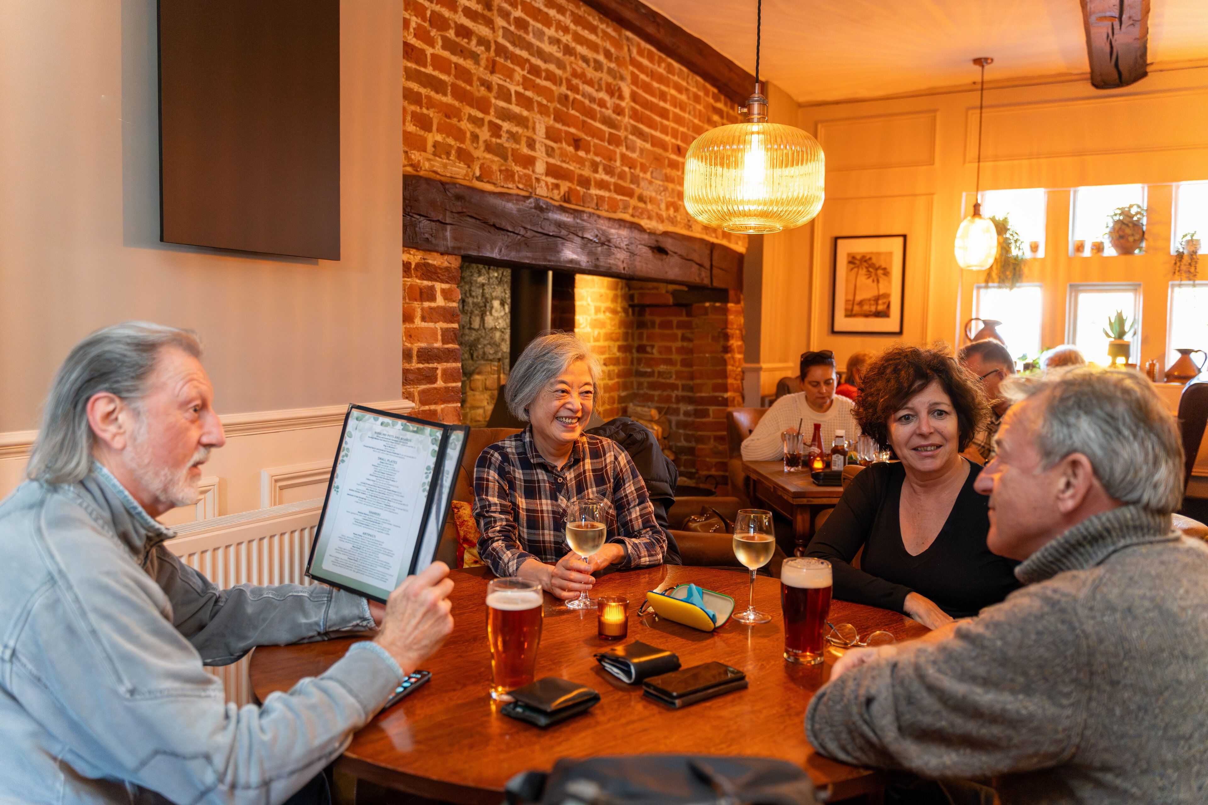 A group of people sitting around a wooden table in a restaurant with brick walls and hanging lights.