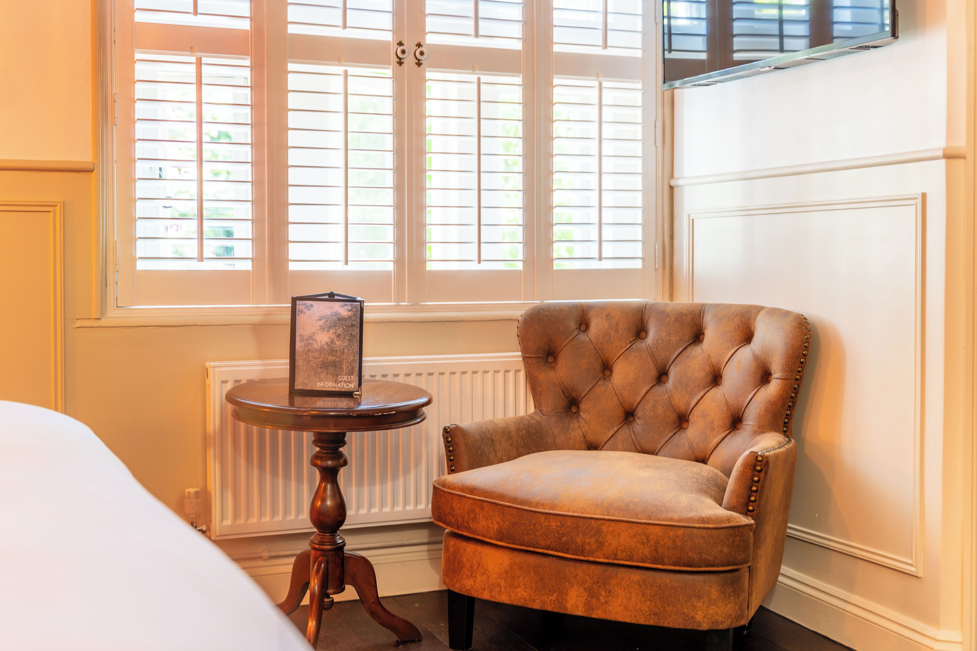 A room with a tufted armchair, a small wooden table with a glass object, and a radiator.