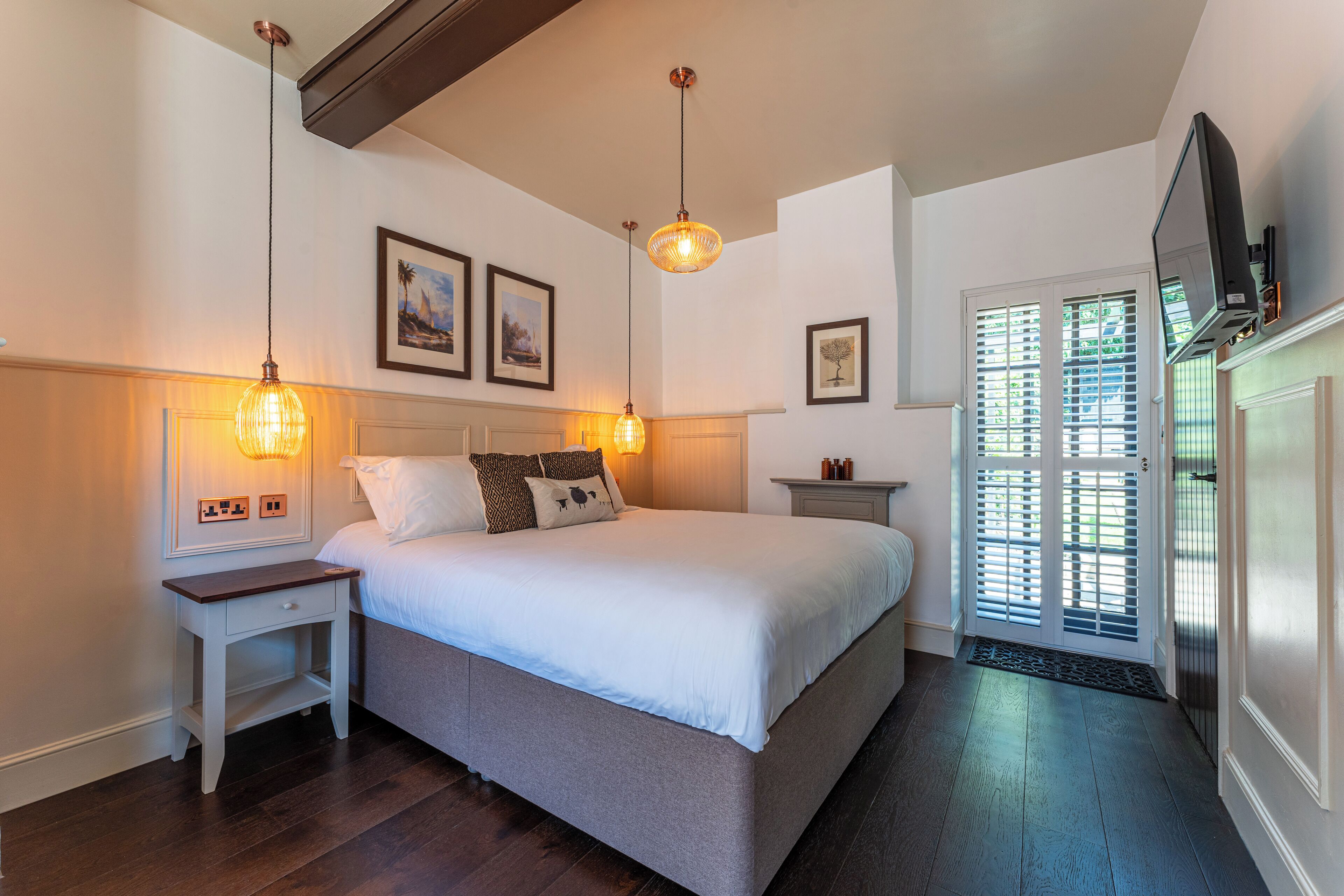A bedroom with a bed, bedside tables, a television, and a door with blinds.