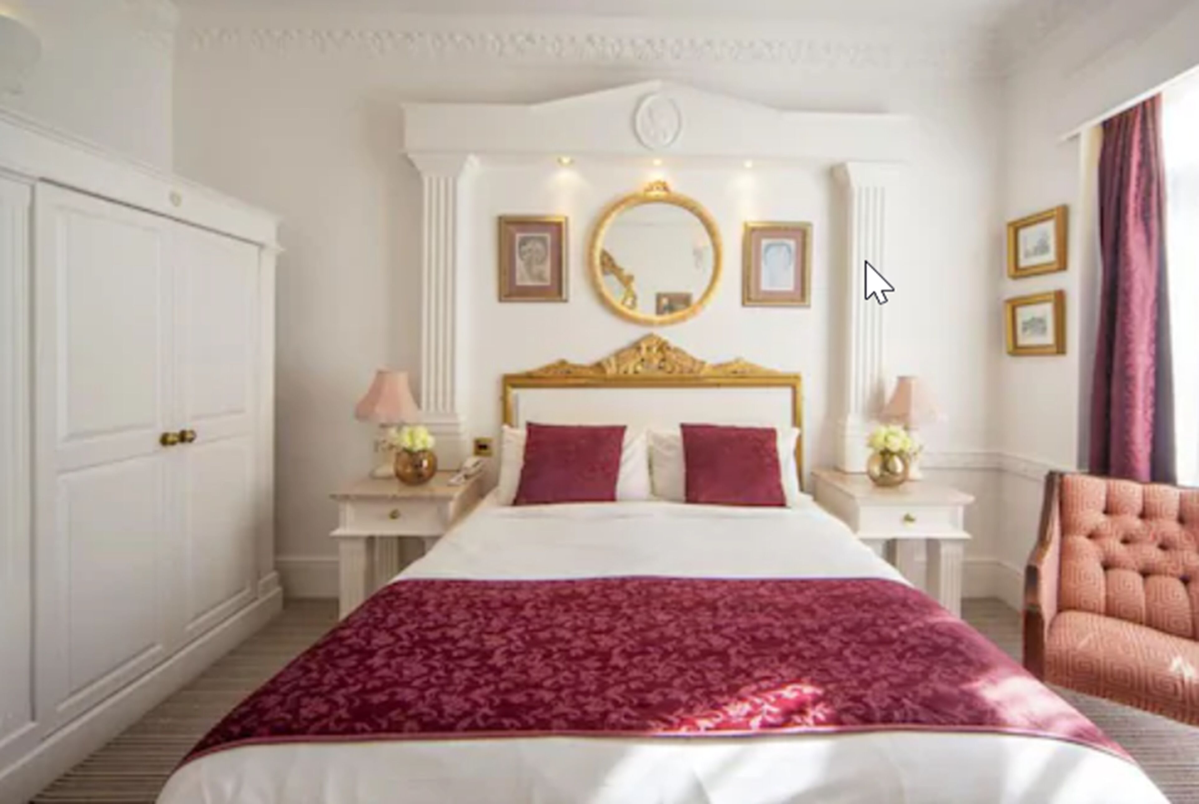 Une chambre d’hôtel avec un grand lit, une tête de lit ornée d’un cadre doré, deux tables de chevet avec des lampes et un grand miroir au-dessus du lit.