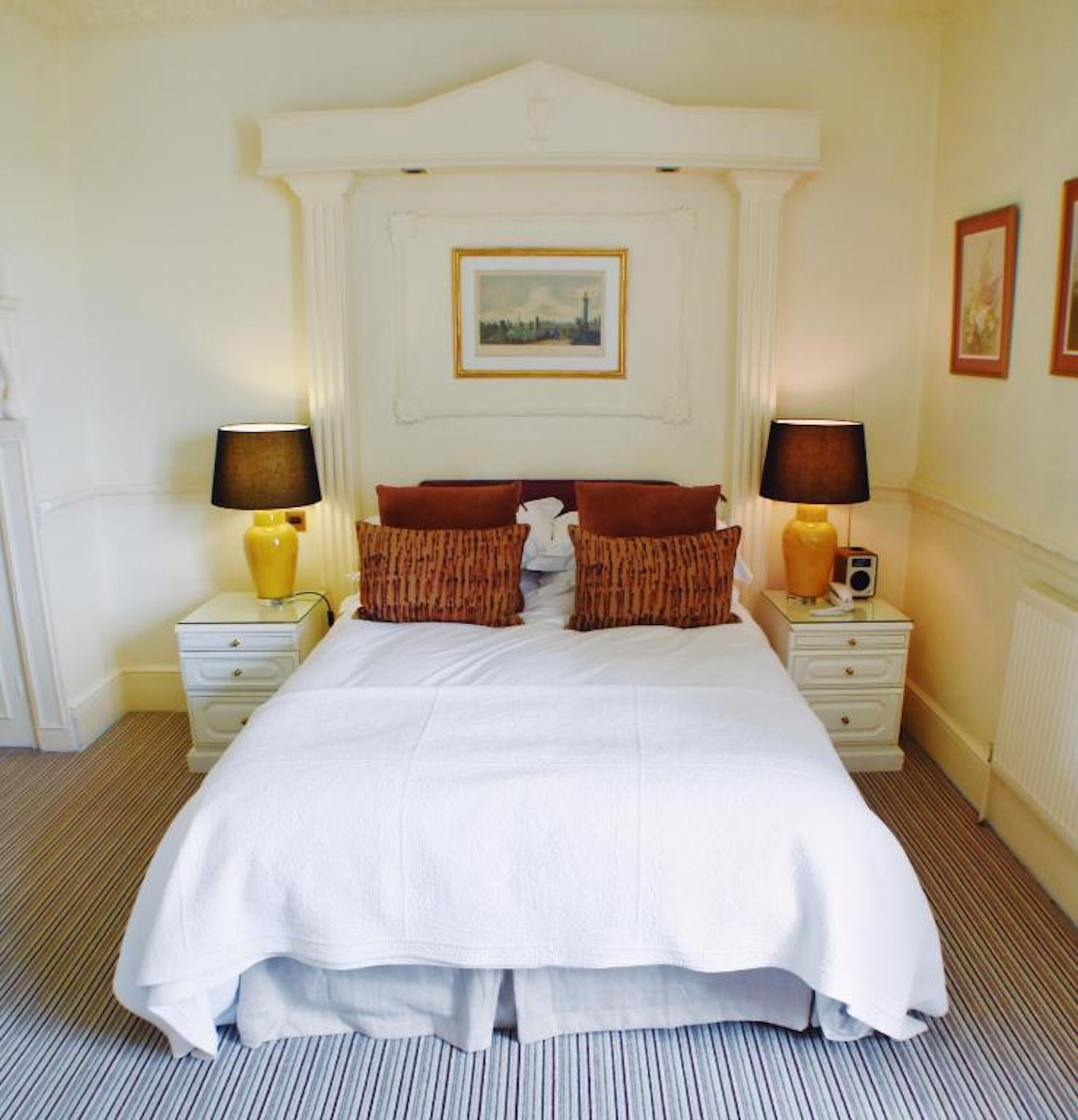 Quarto de hotel bem arrumado, com uma cama grande, duas mesas de cabeceira com abajures e um quadro emoldurado acima da cama.
