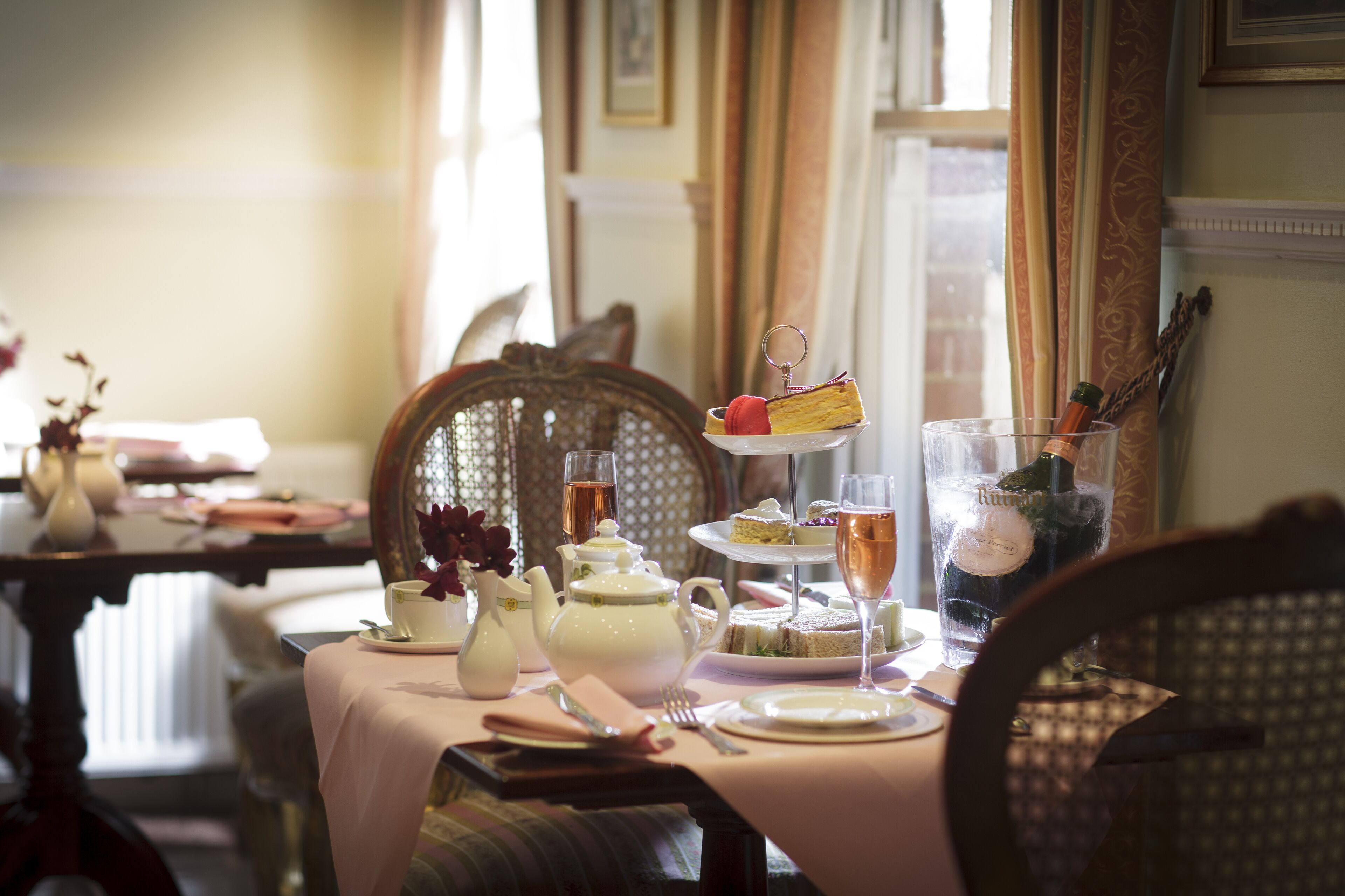 A dining table set with a teapot, cups, a tiered cake, and a glass of champagne.