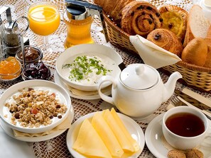 Desayuno con tetera, tazas, cesta de pasteles y un plato de queso.